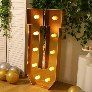 Gold marquee letter "U" with lights in a festive setting.