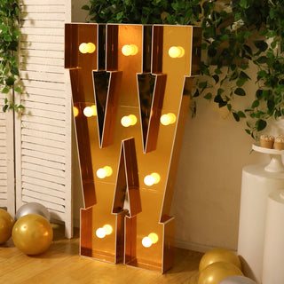 Gold marquee letter "W" with lights, styled in a festive decor setting.