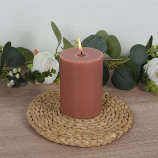 Rustic pink candle on a woven mat with greenery background.