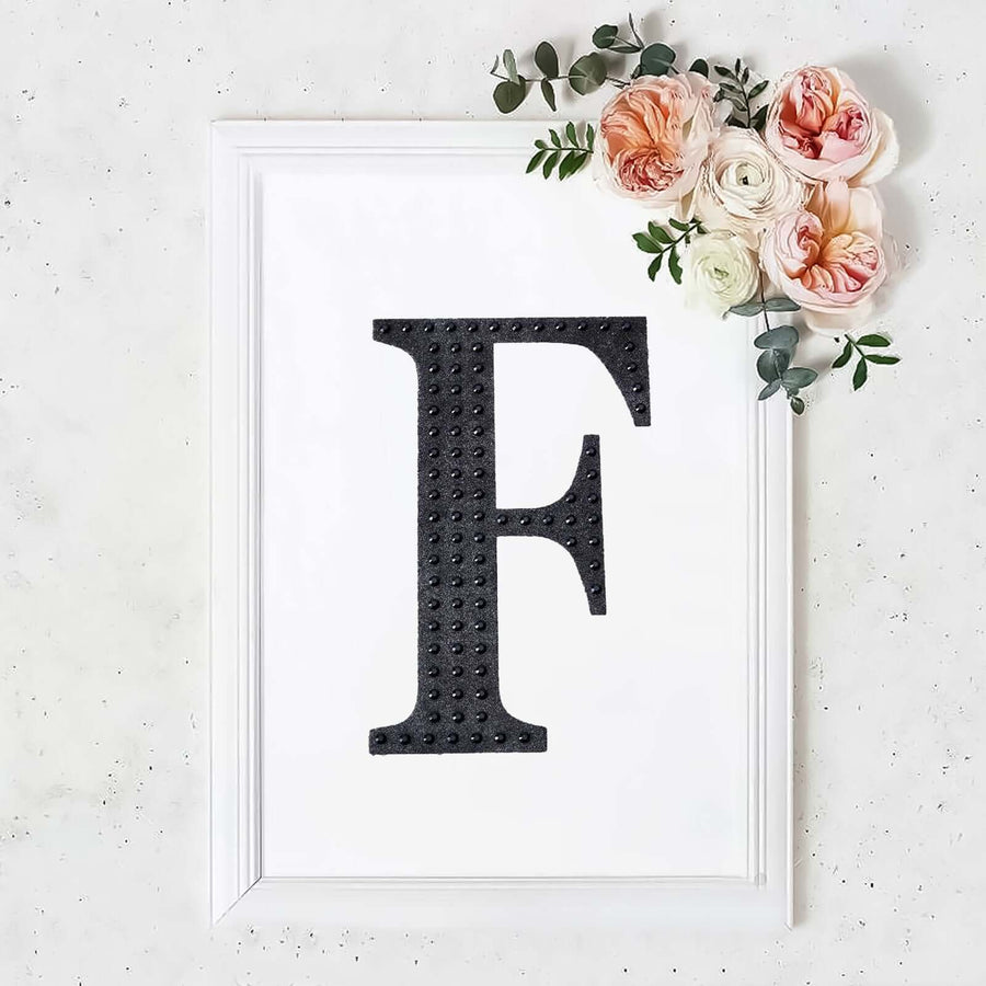 Black letter "F" in a white frame adorned with flowers.