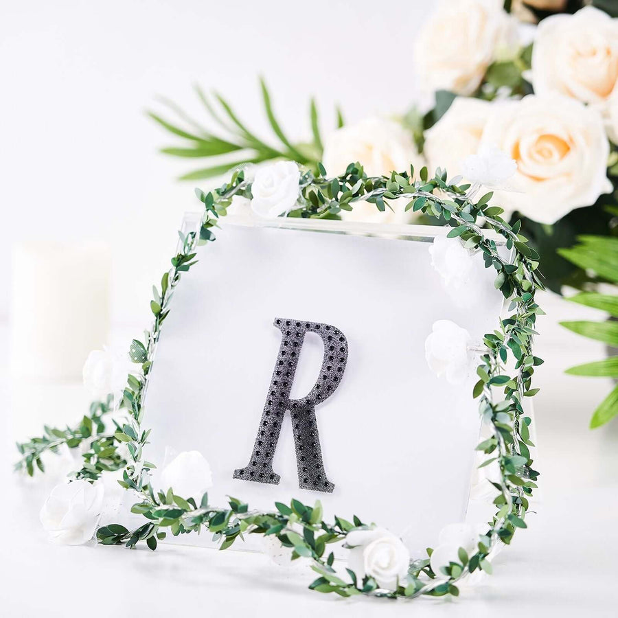 Decorative letter 'R' framed with flowers and greenery on a white background.