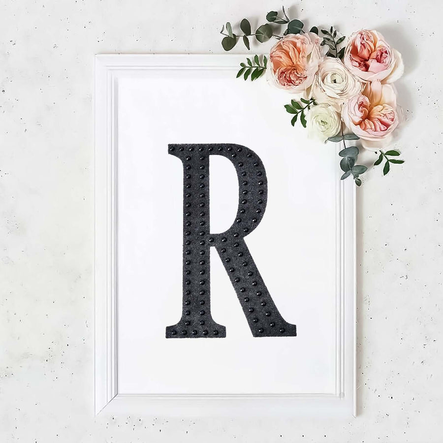 Black letter "R" framed with flowers on a white background.