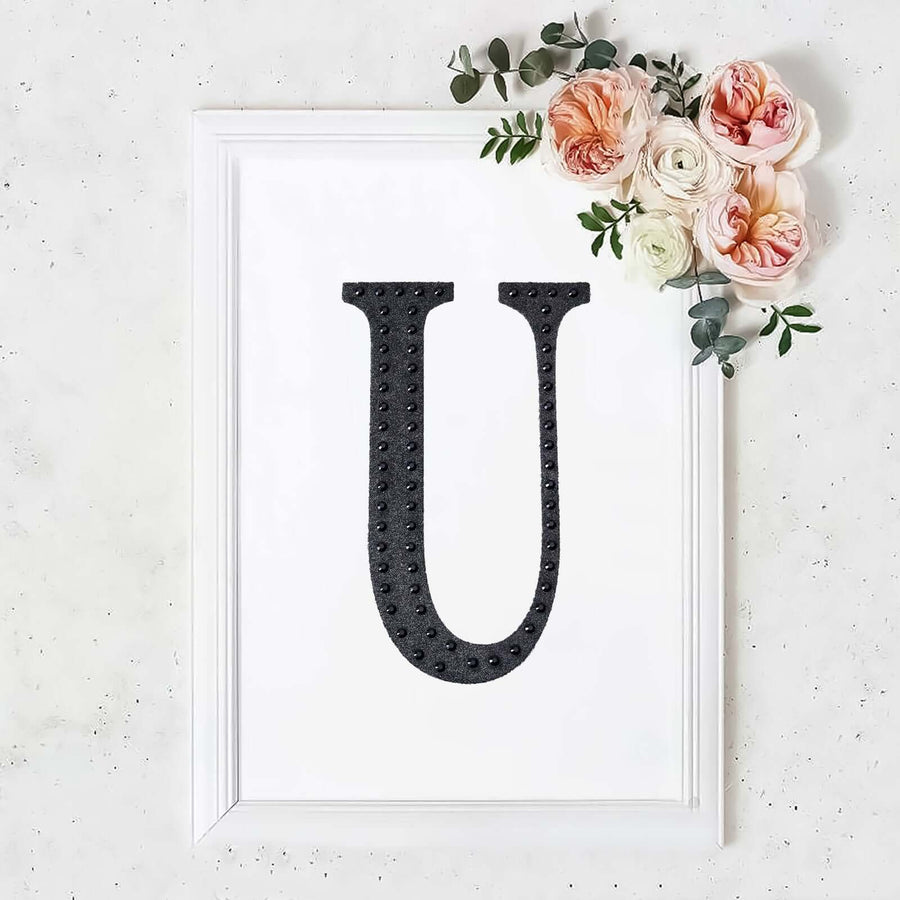 Black letter 'U' art print with floral accents in a white frame.