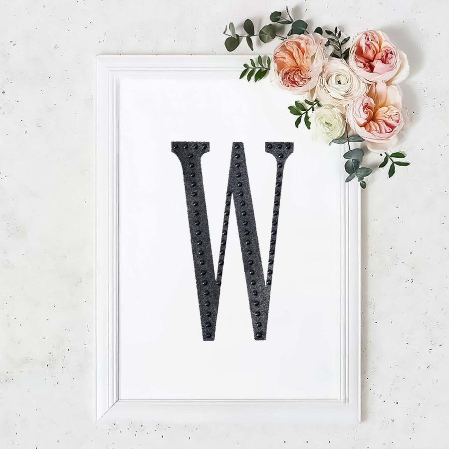 Black letter "W" in a white frame with floral accents.