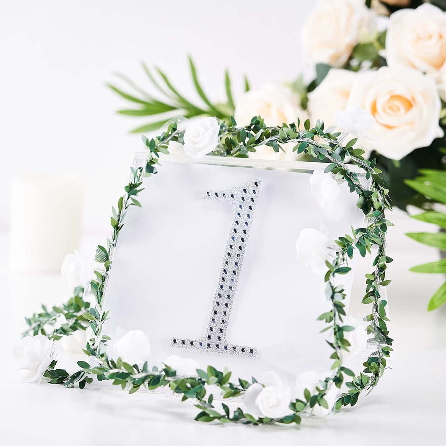 Table number holder with floral decor and rhinestone accent.