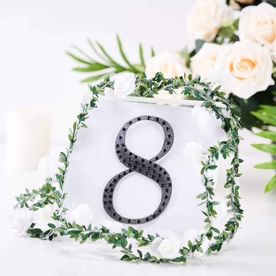 Decorative table number 8 surrounded by greenery and white roses.