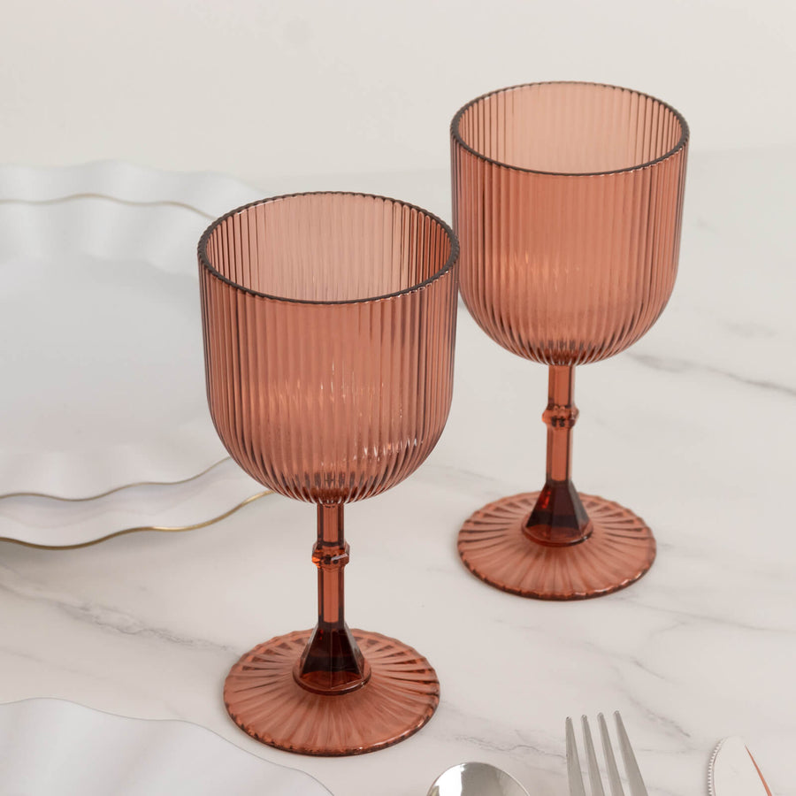 Two elegant ribbed glass goblets in rose color on a marble table.