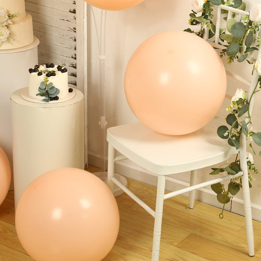 Peach balloons on a chair with a cake and greenery in a styled setting.