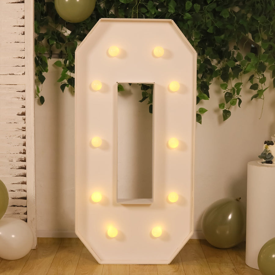 Light-up marquee number zero with warm bulbs against a greenery backdrop.