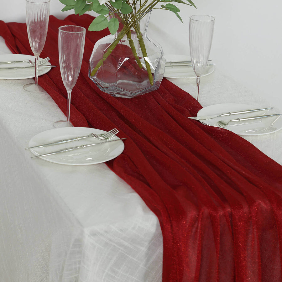 Red table runner on a dining table set with glassware and plates.