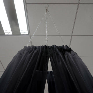 Black sheer curtain hanging from a chain in an indoor setting.