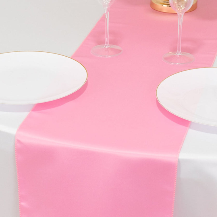 Pink satin table runner on a dining table with white plates and glasses.