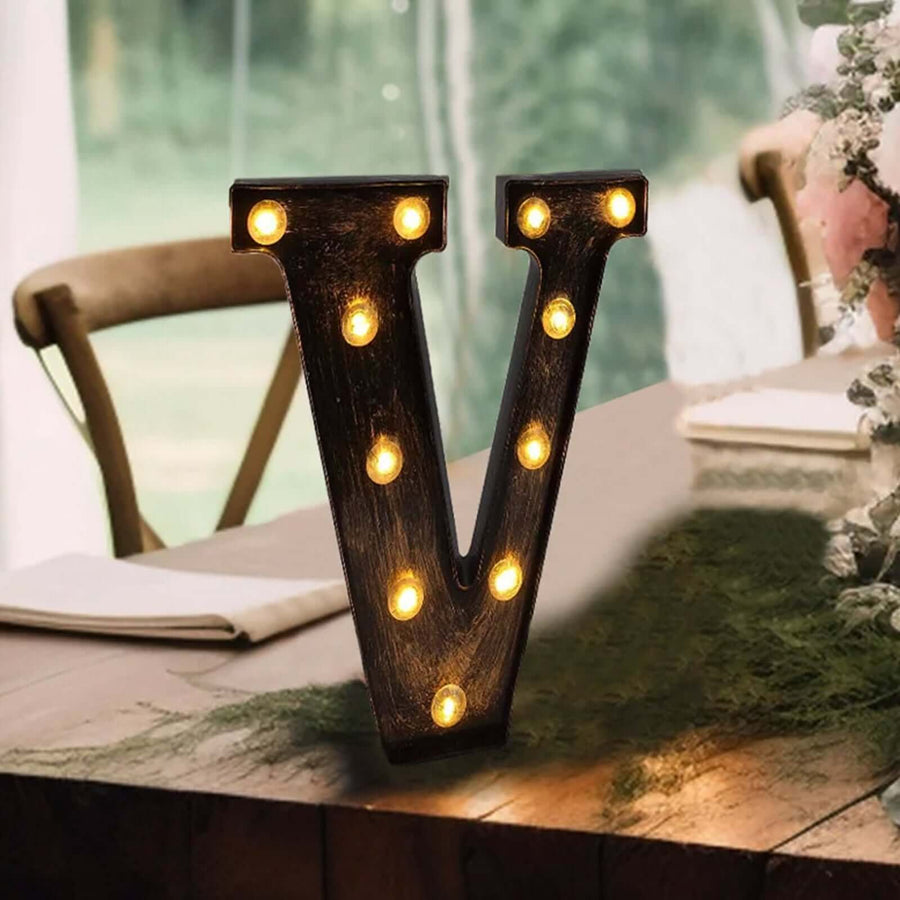 Decorative marquee letter "V" with warm lights on a rustic table setting.
