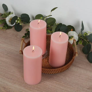 Three pink candles burning on a woven tray with greenery accents.