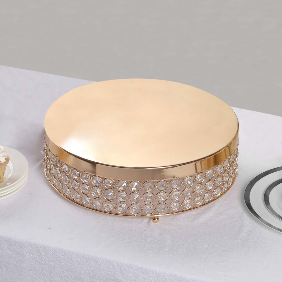 Gold cake stand with crystal embellishments on a plain surface.