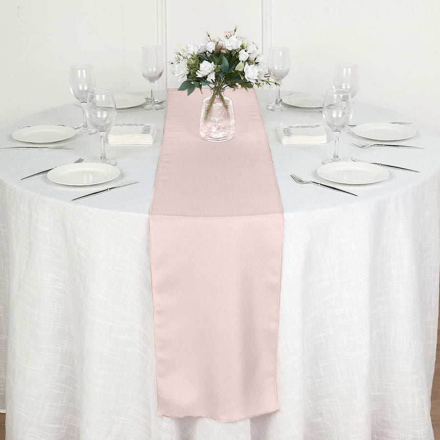 Blush pink table runner on a round dining table with floral centerpiece and dishes.
