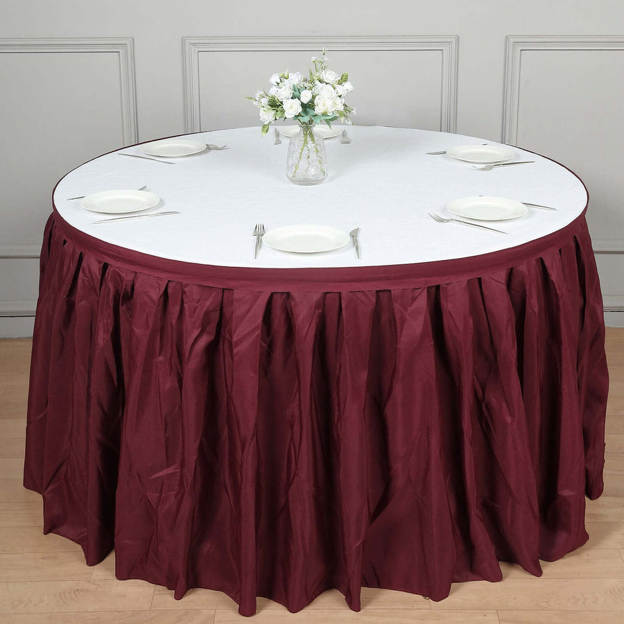 Round burgundy tablecloth draped elegantly on a table with white plates and a floral centerpiece.