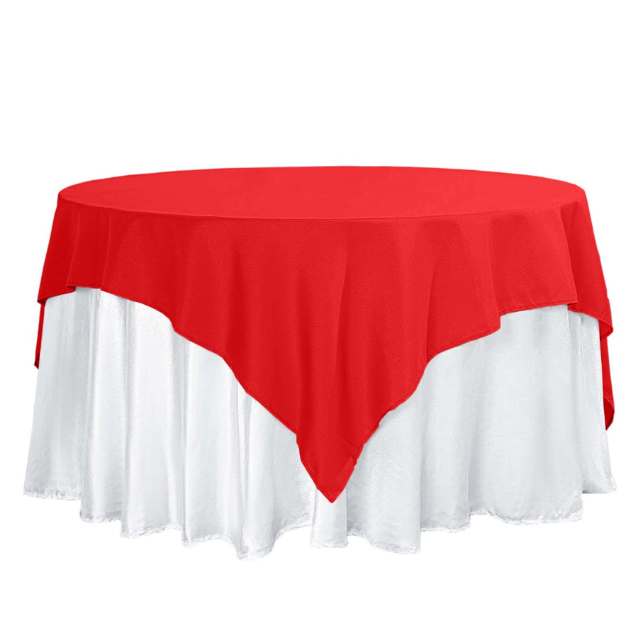 Red tablecloth draped over a white tablecloth on a round table.
