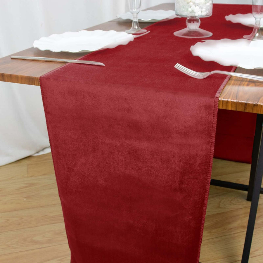 Burgundy table runner on a wooden table setting with plates and cutlery.