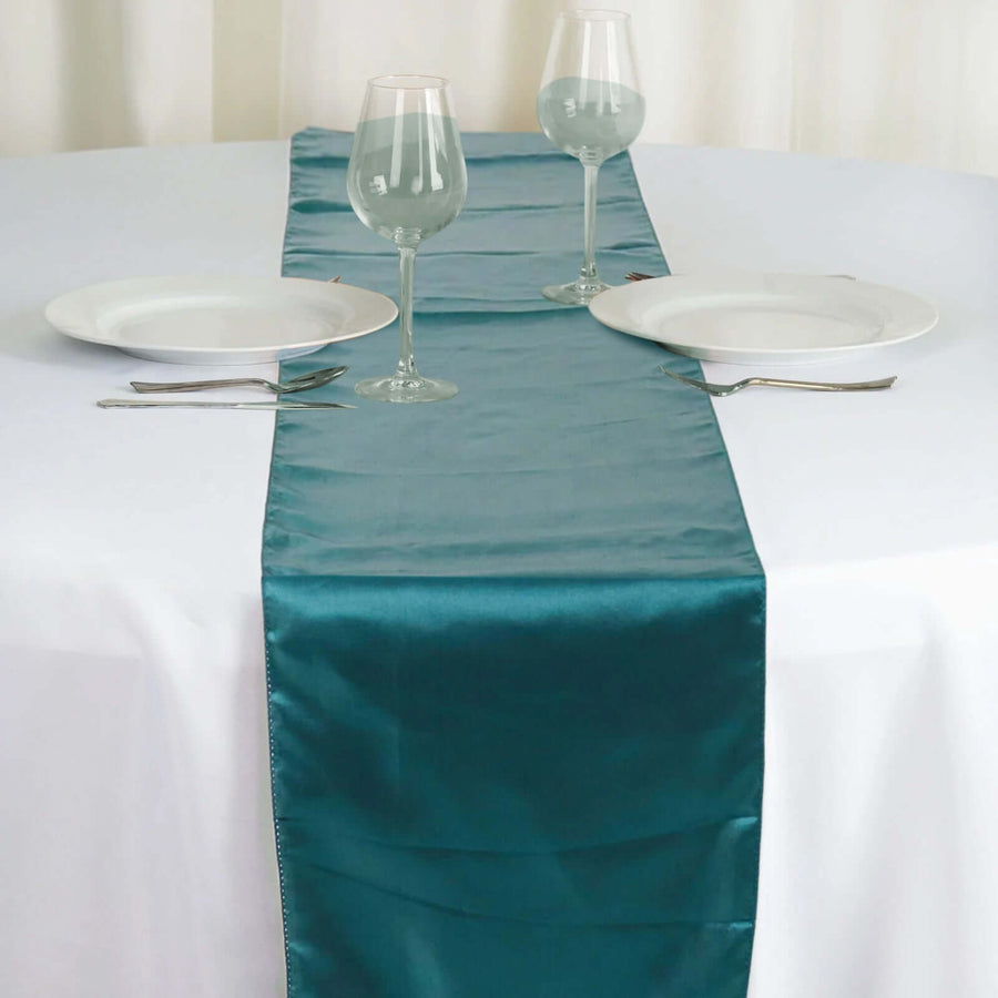 Teal satin table runner on a white table setting with plates and glasses. #whtbkgd