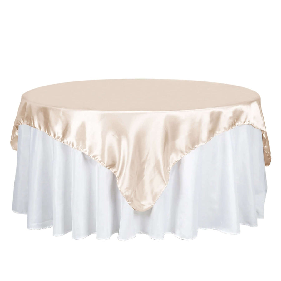 Round table with a beige satin tablecloth and white skirt.