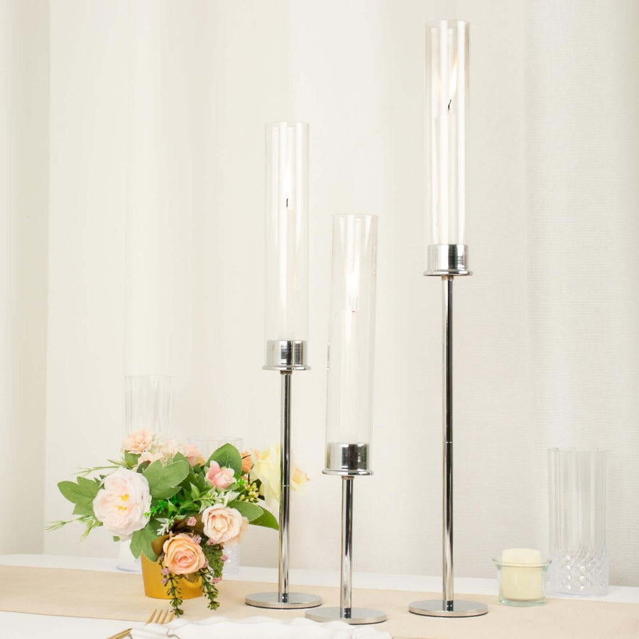 Elegant candle holders in varying heights with modern design and floral arrangement.