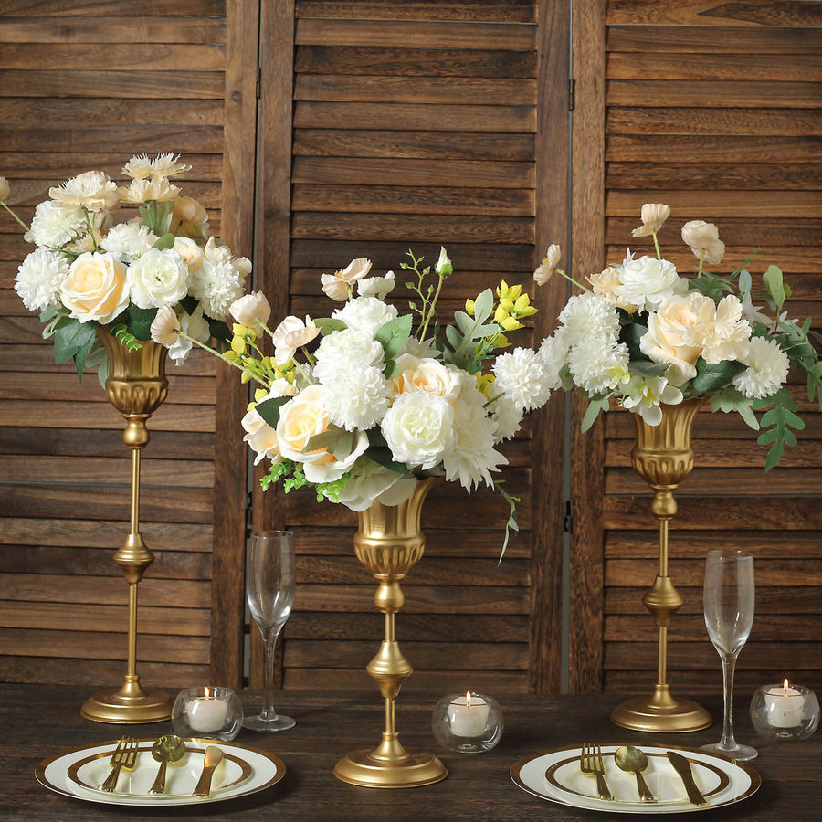 Elegant floral arrangements in gold vases on a wooden table setting.