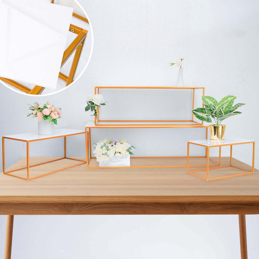 Decorative display stands with gold frames and white surfaces on a wooden table.
