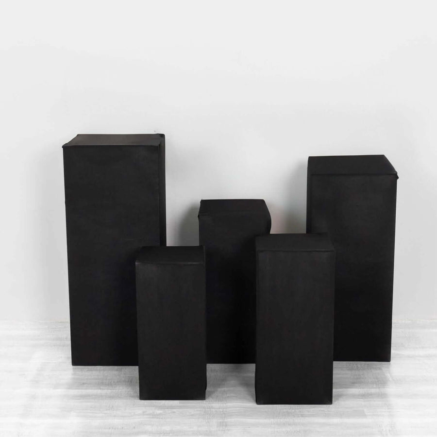 Black geometric display pedestals in various heights on a plain background