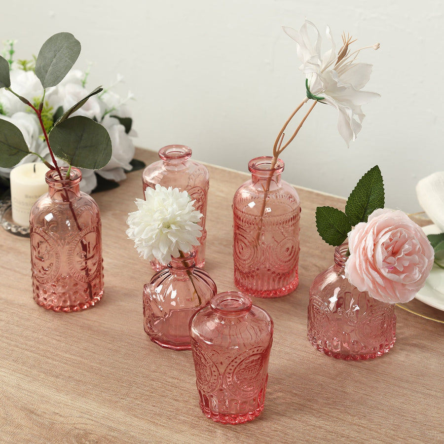 Set of pink glass vases with flowers on a wooden table.
