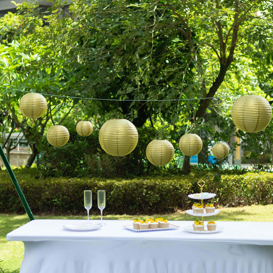 Gold paper lanterns hanging in a garden setting with a table and dessert stand.