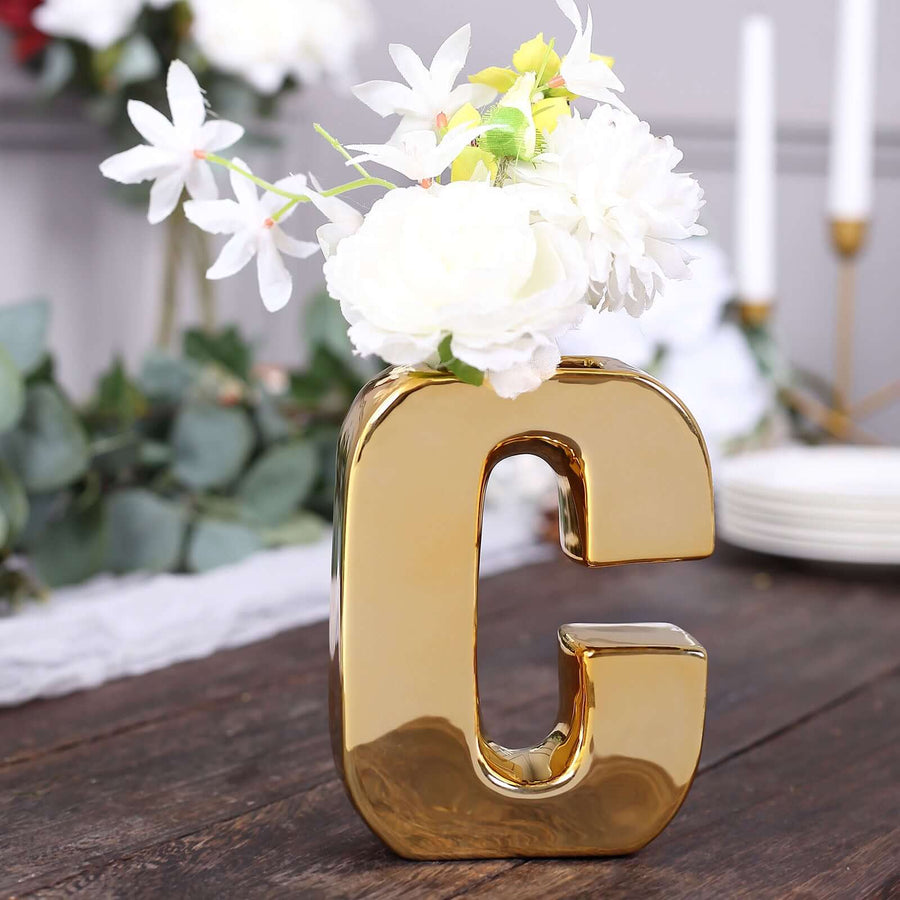 Gold letter "G" vase with white flowers on a wooden table.
