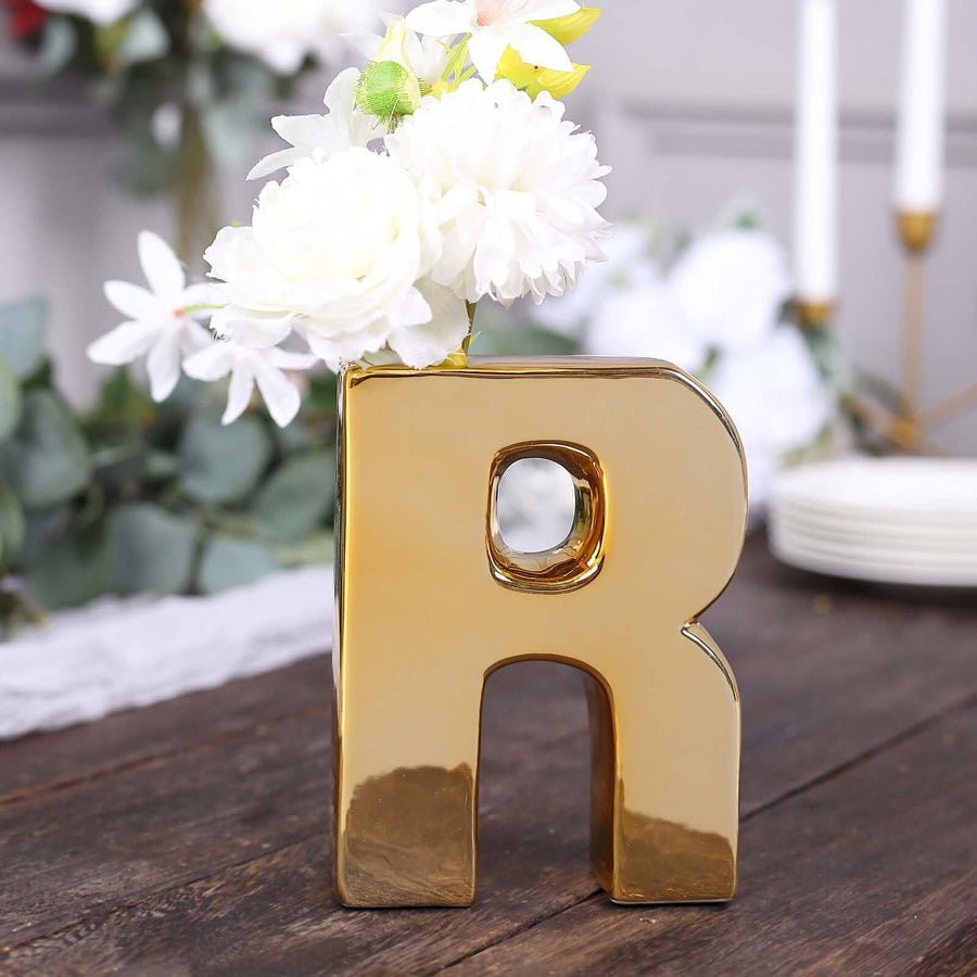 Gold letter "R" vase with white flowers.