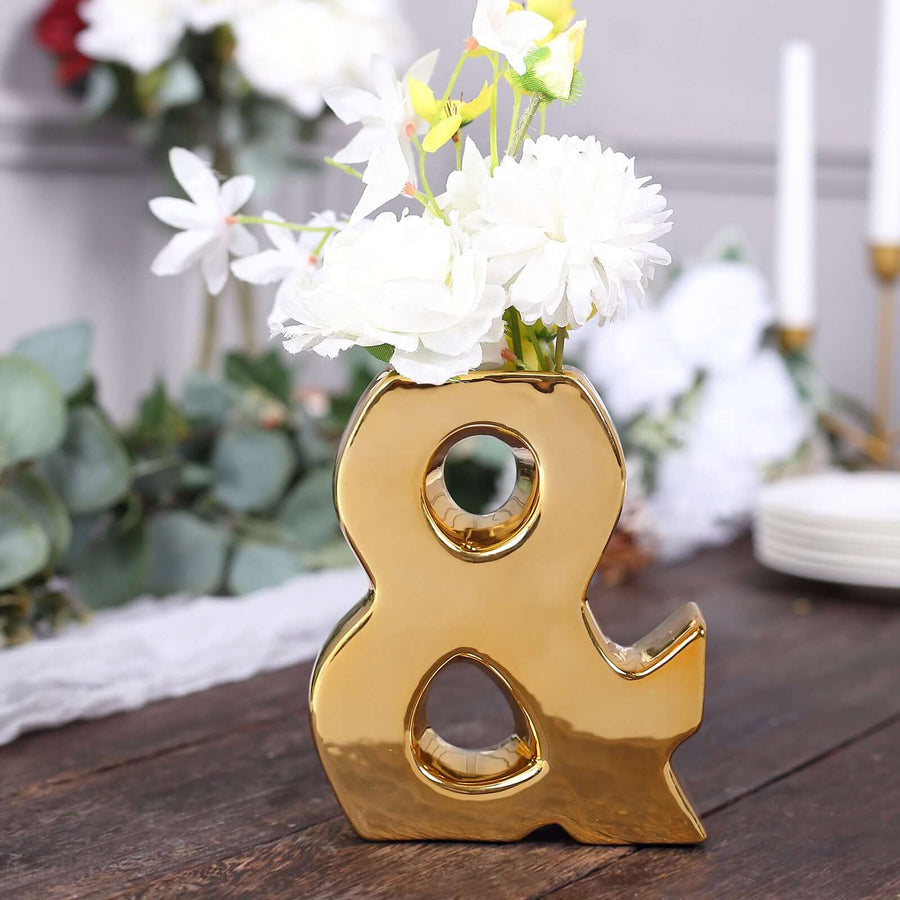 Gold ampersand vase with white flowers on a rustic wooden table.