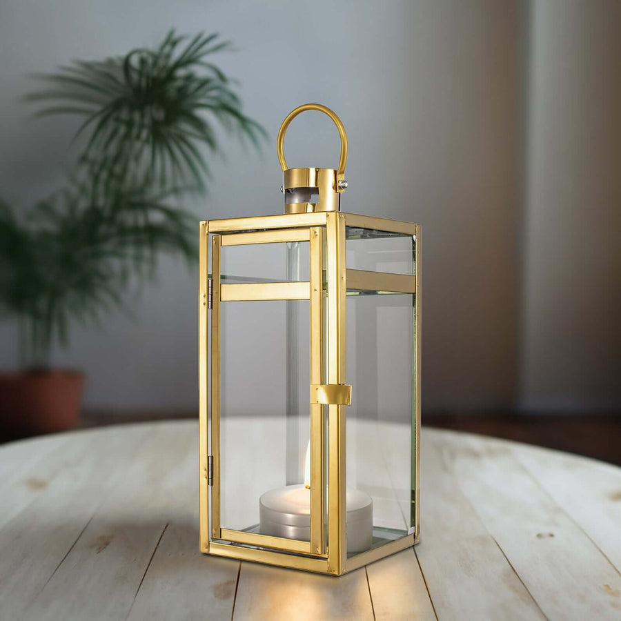 Gold lantern with glass panels and a candle, set on a wooden table.