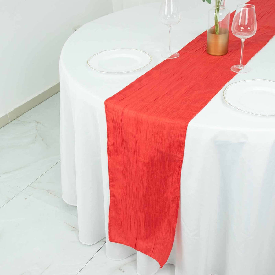Red table runner on a round table set for dining with glassware.