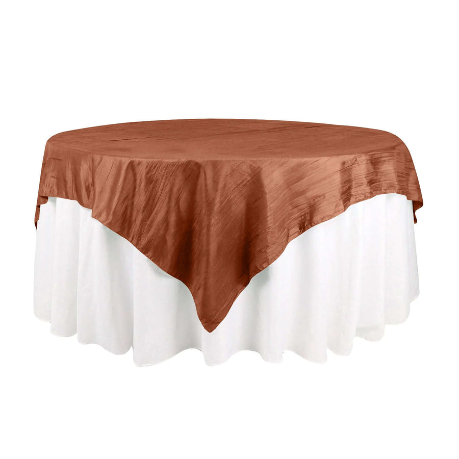 Round table with a brown satin tablecloth on a white skirted base.