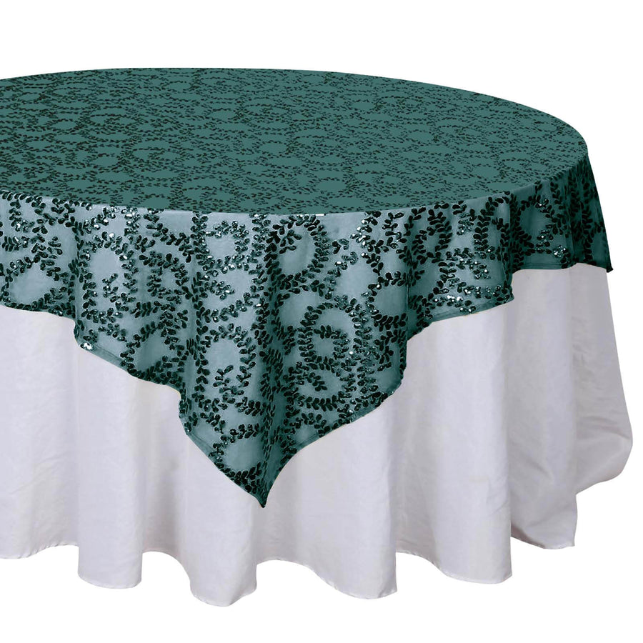 Green sequin tablecloth with intricate leaf pattern on a white table.
