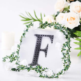 Decorative letter "F" with floral accents and greenery on a white background.