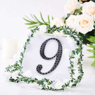Black number 9 surrounded by greenery and white flowers on a clear base.