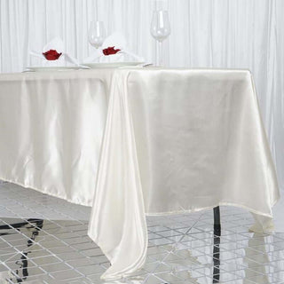 Elegant ivory satin tablecloth draping over a table with decorative touches.
