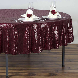 Burgundy sequin tablecloth on a dining table set with plates and napkins.