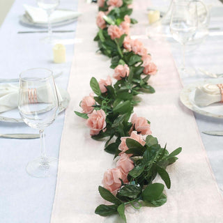 Pink rose garland centerpiece on a dining table with glassware and plates.