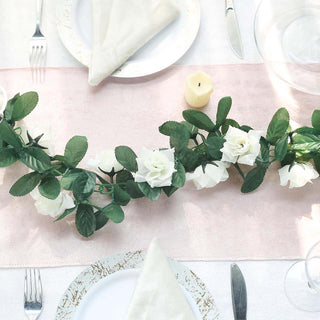 White rose garland centerpiece on a pink table runner with dining setup.