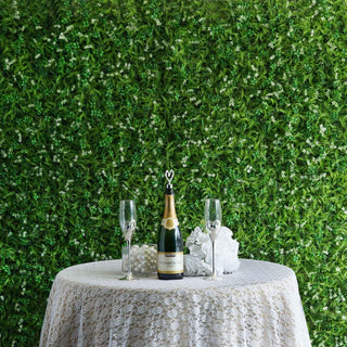 Champagne bottle with flutes on a lace table against a green floral backdrop.