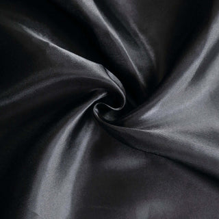 Black satin fabric with a smooth texture in a swirling pattern.