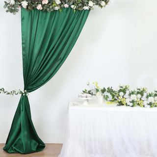 Green satin drapery with floral arrangement on a white table in a decorated setting.
