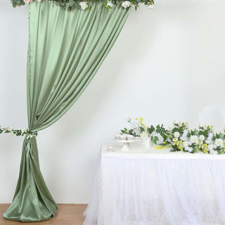 Green satin drapery and floral arrangement on a table in a bright setting.