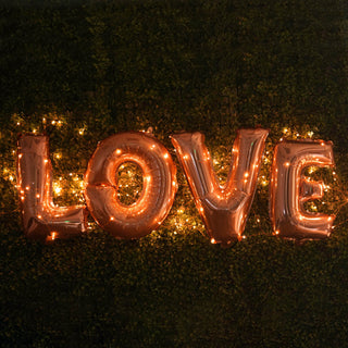 Rose gold "LOVE" balloon letters with fairy lights on a green backdrop.
