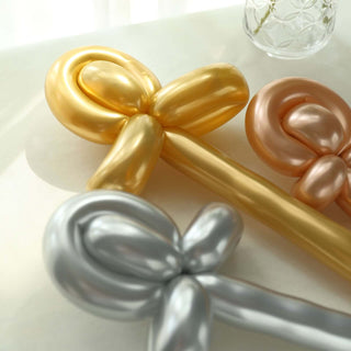 Three shiny balloon bows in gold, silver, and rose gold on a light surface.